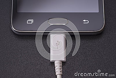 Black smartphone on black background with white cable Stock Photo