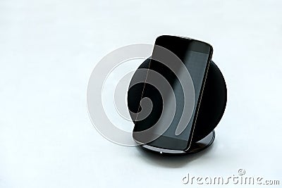 Black smartphone charged by wireless charger on gray wooden background. Wireless charge or digital technology concept Stock Photo