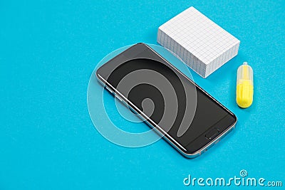 Black smartphone, a pile of scratch paper and one yellow textliner on blue background isolated Stock Photo