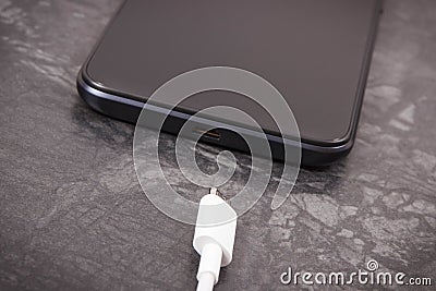 Black smartphone and unconnected cable of charger. Telephone charging Stock Photo