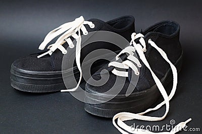 Black sneakers with white untied laces on a black background Stock Photo