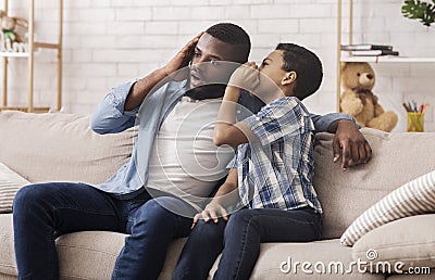 Black Son Sharing Secret With Dad, Whispering To His Ear Stock Photo