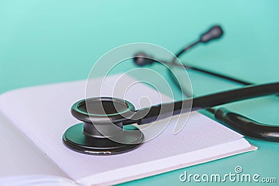 Black stethoscope and white notebook on pastel green background Stock Photo