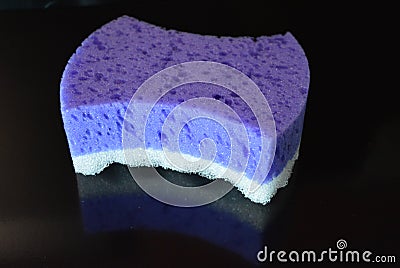 On a black stylish glossy background is a female purple sponge for a body of purple and white with reflection Stock Photo