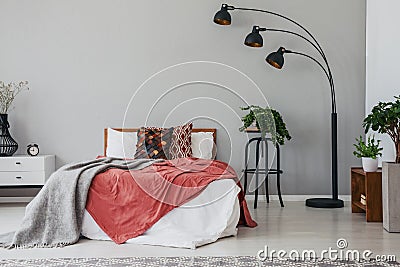 Black stylish lamp in elegant bedroom interior with comfortable double bed, plants, and bedside table Stock Photo