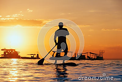 Black sunset silhouette of paddle boarder standing on SUP Stock Photo