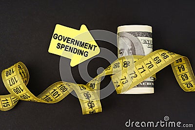 On a black surface there are dollars wrapped in measuring tape and stickers with the inscription - government spending Stock Photo