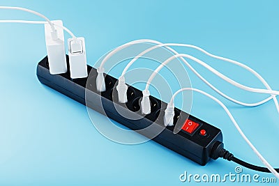 Black surge protector with a red button and connected white wires of electrical appliances on a blue background. Stock Photo