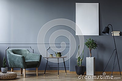 Black table between green armchair and plants in grey interior w Stock Photo