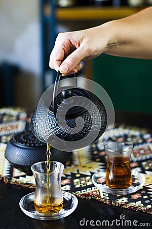 Black tea and teapot in hand, Turkish tea glasses, and old iron teapot Stock Photo