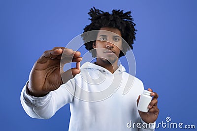 Black teenager holding jar of tablets and showing one pill over blue studio background, selective focus Stock Photo