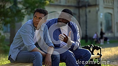 Black teenager male ignoring scolding dad sitting on campus bench, conflict Stock Photo
