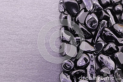 Black tourmaline jewel heap on black stone half background. Pile mineral pebbles texture. Stock Photo