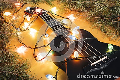black ukulele guitar and christmas decorations on the dark background. hawaiian guitar with lighted garland on dark background. Stock Photo