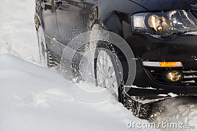 Black vehicle moving through the deep snow skidding, car's wheel spin and spew up pieces of snow it attempts to gain Stock Photo