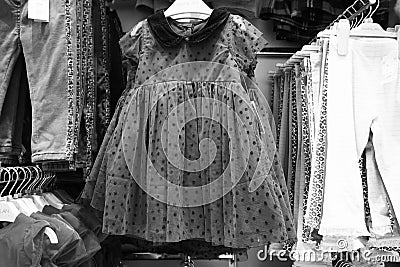 Black and White image of Children clothes hanging on hangers in the shop. Colourful kid blouses and shirt hanging on the cloth Editorial Stock Photo