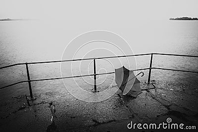 Black and white image of forgotten umbrella a rainy day by the water Stock Photo