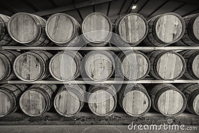 A black and white image of a front on view of a row of stacks of traditional full whisky barrels, set down to mature, in a large Stock Photo