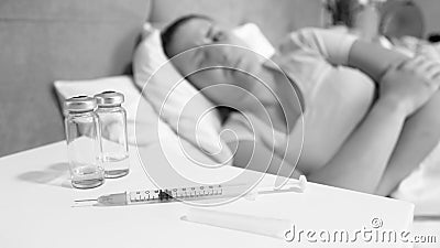 Black and white image of syringe and ampules on bedside table against sick woman lying in bed Stock Photo