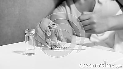 Black and white image of young woman lying in bed taking ampules with medicines and syringe from bedside table Stock Photo