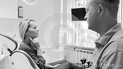 Black and white image of young woman sitting in dental clinic and showing aching tooth Stock Photo