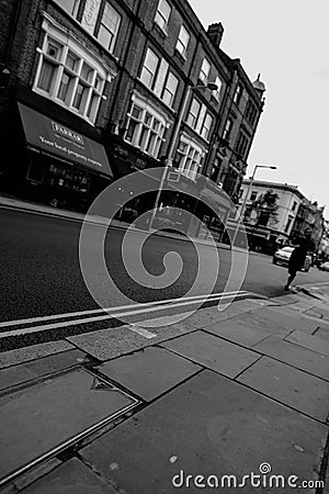 Black and White, monochrome, tilted view of city street with double yellow lines and single pedestrian being passed by single car Editorial Stock Photo