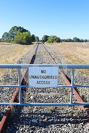 A black and white No Unauthorised Access warning sign on the fence of a closed railway line Stock Photo