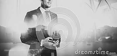 Black white photo of businessman holding smartphone. Double exposure, city on the background. Wide Stock Photo