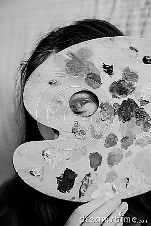 A black-white photo capture an artist peering into a hole in her paint palette where oil paints have been mixed. A new perspective Stock Photo