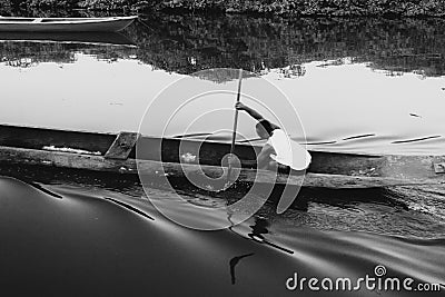 Black and white photograph of a fisherman paddling his canoe on Editorial Stock Photo