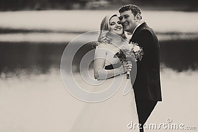 A black and white picture of a happy wedding couple standing behind a lake Stock Photo