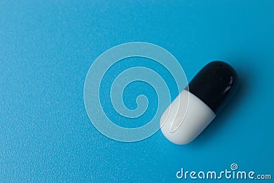 Black and white pill close up on blue background, copy space. Pharmaceutical industry Stock Photo