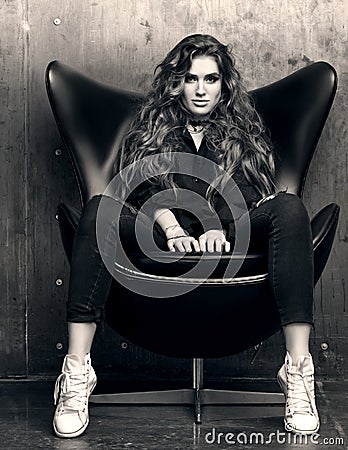 Black and white portrait of the imperious young woman sitting in the black chair. Stock Photo