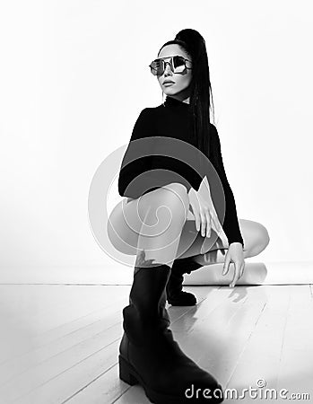 Black and white portrait of sexy brunette woman in black string bodysuit, brutal shoes and sunglasses sitting squatted Stock Photo