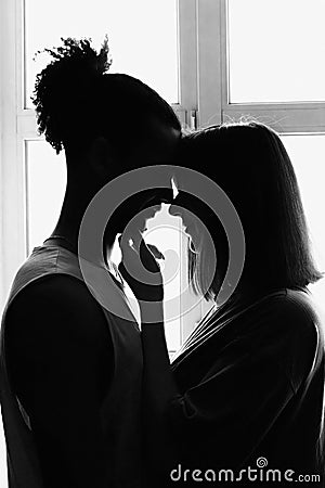 Black and white portrait, silhouette of a multiracial couple, boyfriend and girlfriend face to face, stand at the window Stock Photo