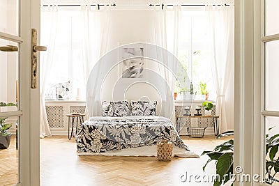 Black and white poster above bed with patterned pillows in bright spacious bedroom interior. Real photo Stock Photo