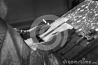 Black and white Priest praying in the church holding holly bible and cross with candles Stock Photo