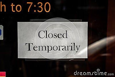 A black and white printed paper closed sign taped to a temporarily shut down business storefront glass window or door due to the Stock Photo