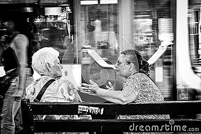 Black and white shot of two elderly females sitting side-by-side on a park bench conversing. Editorial Stock Photo