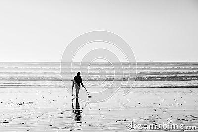 Black and white silhouette of a male using a metal detector searching for treasure at low tide Stock Photo