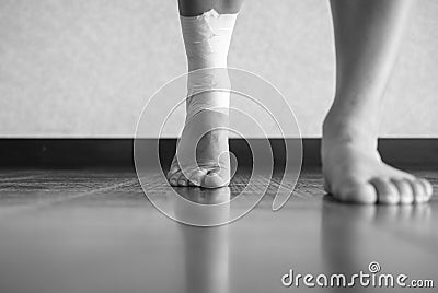 Black and white version of Athlete walking forward with an ankle injury and ankle tape job Stock Photo