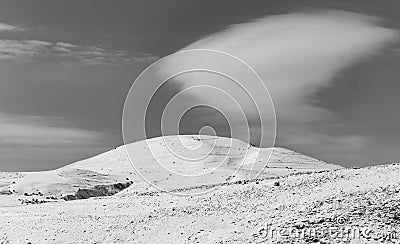 Black and white winter landscape of a snow caped mountain and a huge white cloud floating above it Stock Photo