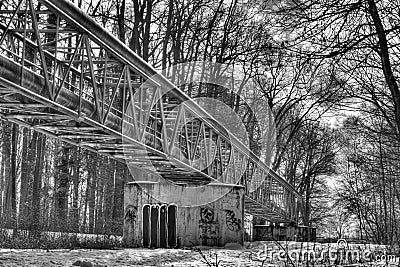 A black and white winter photo of a metallic structure supporting various pipes on concrete blocks running through a forest Stock Photo