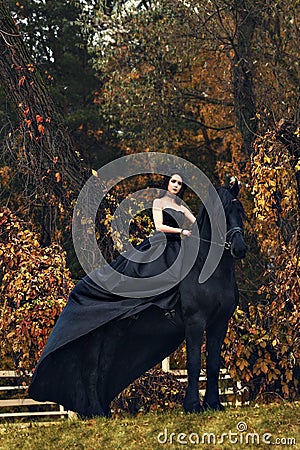 Black witch queen horseback on a black horse in a gloomy grim dark forest as in a horror scary fairy tale Stock Photo