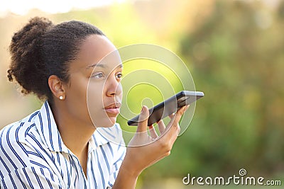Black woman dictating text on phone in a garden Stock Photo