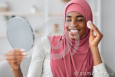 Black Woman In Hijab Holding Mirror And Cleaning Face With Cotton Pad Stock Photo