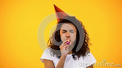 Black woman in party hat blowing noisemaker, celebrating birthday, holiday party Stock Photo