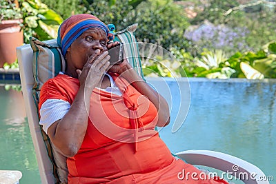 Black woman with surprised expression on her face and holding her hand to her mouth while talking on a cellphone. Stock Photo