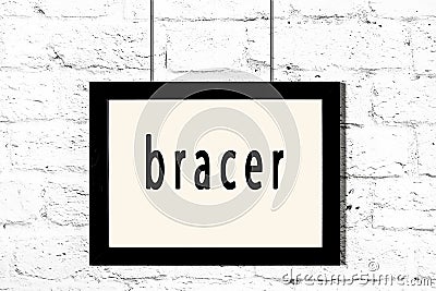 Black frame hanging on white brick wall with inscription bracer Stock Photo