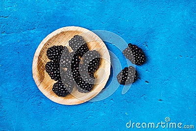 Blackberries on a wooden plate on a textured classic blue background Stock Photo